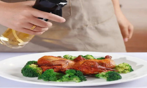 "Person holding a glass of beer with a plate of roasted chicken and broccoli in the foreground, capturing a cozy dining moment."