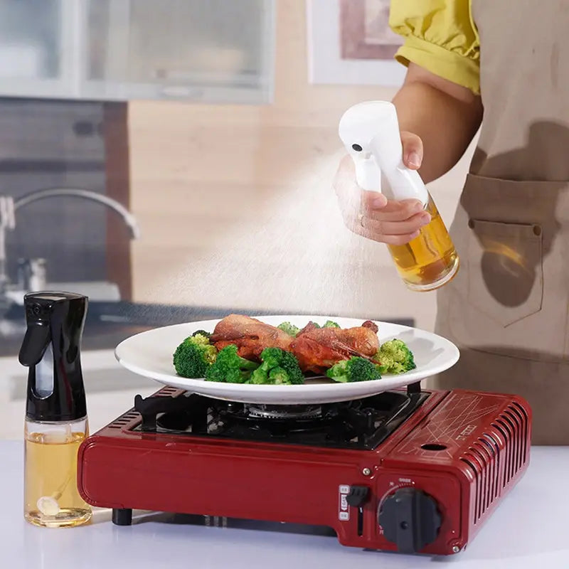 "Person using a spray bottle to apply oil or seasoning over a plate of food on a portable stove in a modern kitchen setting."