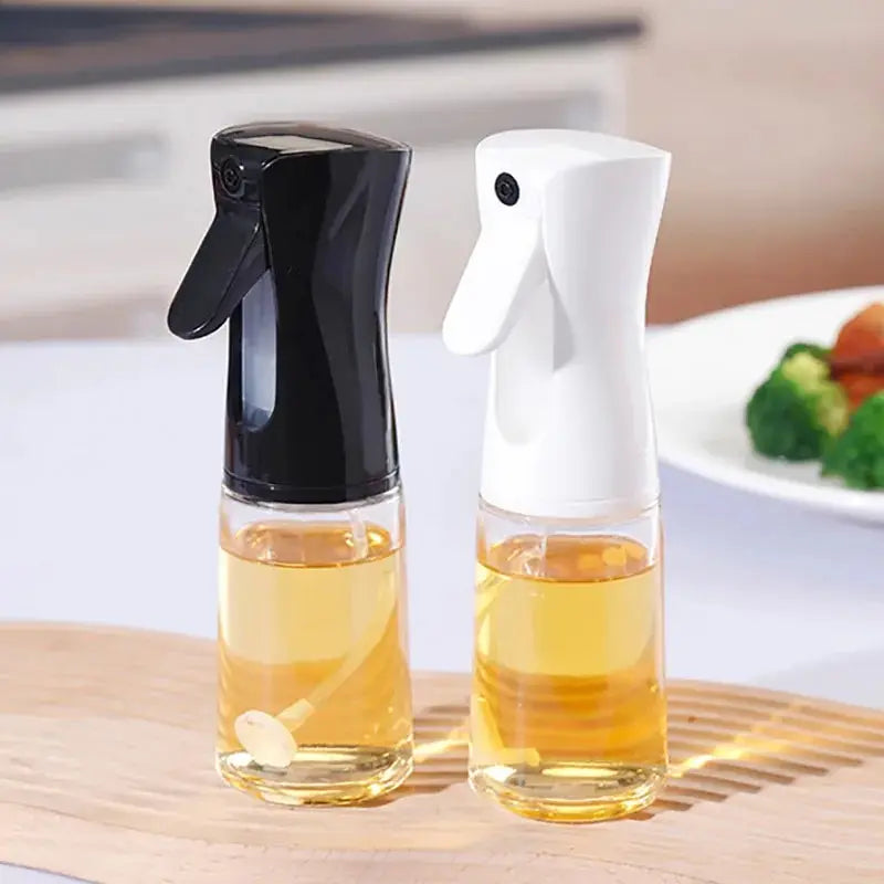 "Two glass spray bottles with black and white nozzles placed side by side on a wooden surface, ideal for kitchen oils or cleaning solutions."