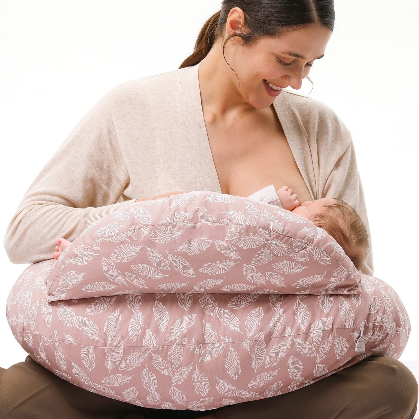 A mother is sitting on the floor, using a multifunctional nursing pillow to hold her baby comfortably for breastfeeding.